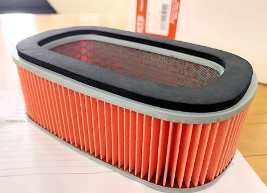 Car air filter with orange pleated design and black rim on a white surface.