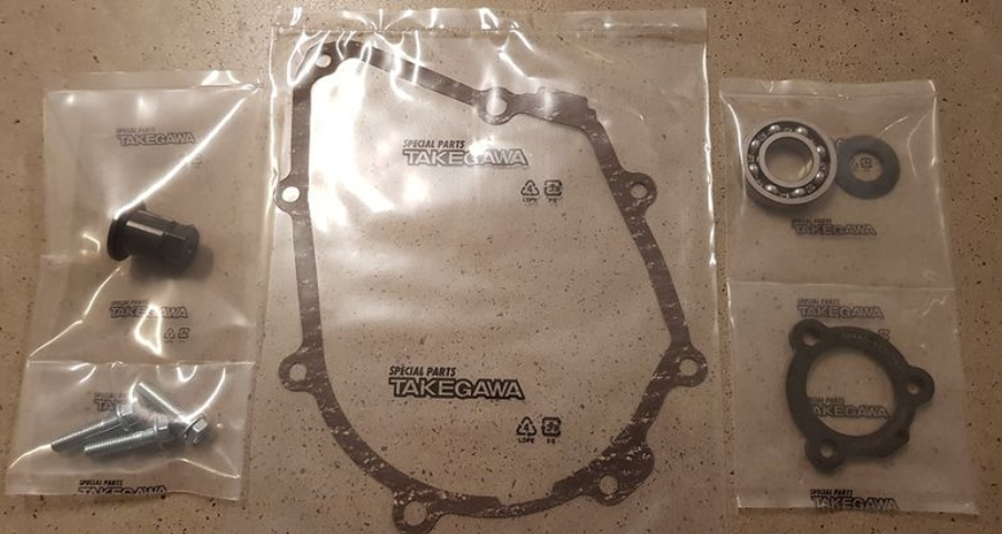 Mechanical parts including a gasket and bearings on a beige surface with 'Takegawa' branding.