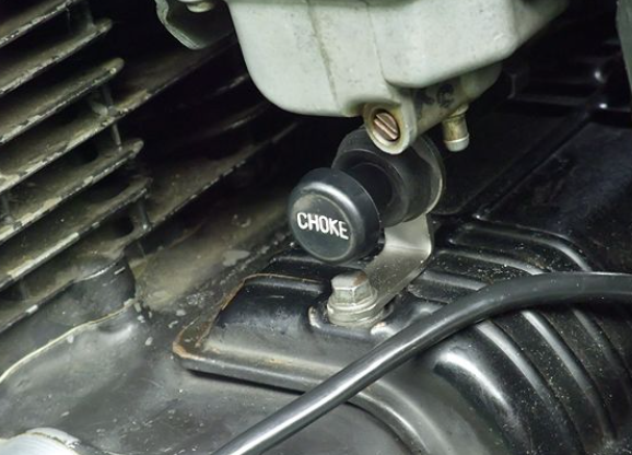 Close-up of a choke lever on an engine, with visible text 'CHOKE'.