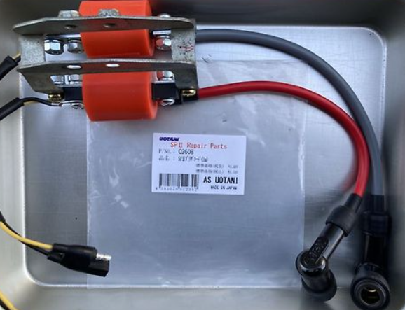 Metallic repair part with red and black cables on a labeled surface