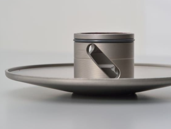 Metallic cylindrical object with a handle on a gray background