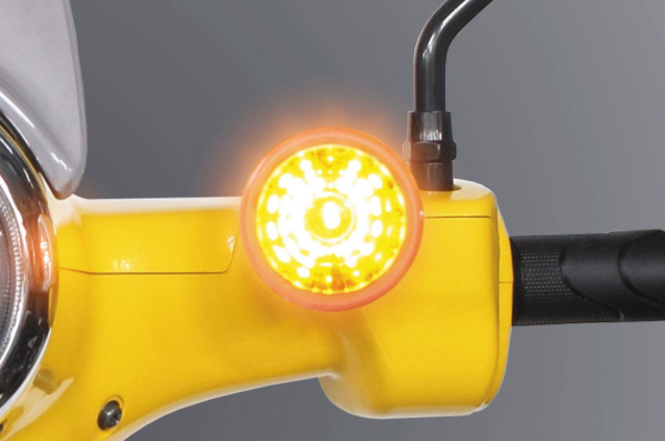 Close-up of a yellow motorcycle handlebar with an illuminated turn signal against a gray background