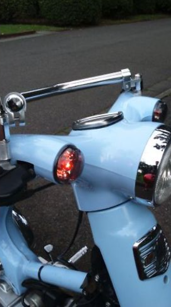 Close-up of a light blue motorcycle with chrome details on a road.