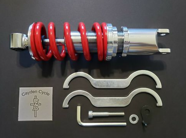 Motorcycle shock absorber with red springs and metal components on a black background, featuring 'Cayden Cycle' branding.