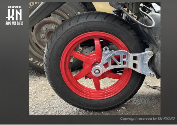 Close-up of a motorcycle wheel with a red rim and black tire on a textured surface.