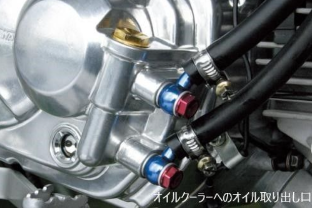 Close-up of a motorcycle engine with oil draining valve and hoses.