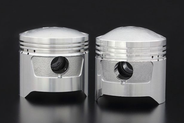 Two metallic piston-like objects on a reflective surface with a dark background