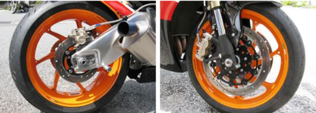 Close-up of a motorcycle wheel with orange rim and metal components on a road.
