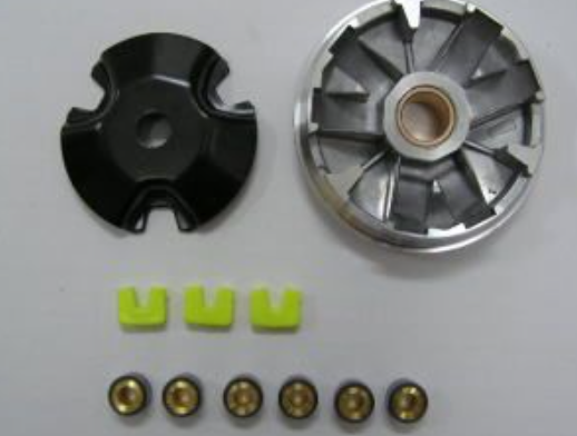 Mechanical parts including a black component, a silver metallic component, and small gold and green items on a light gray background.