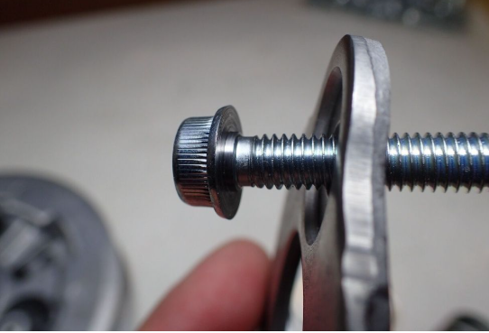 Close-up of a metal screw and washer held by a hand against a blurred background