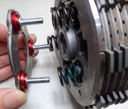 Close-up of mechanical components with a hand holding a red and silver metal piece.