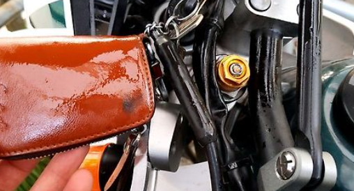 Close-up of a motorcycle brake lever with a brown leather wallet and keys in the foreground.