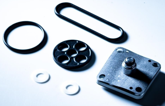 Mechanical components including a black rubber O-ring, a metal washer, and a metallic bracket on a light gray background.
