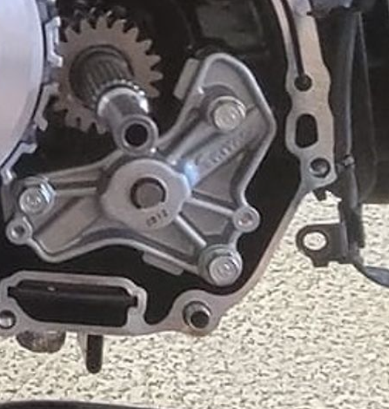 Close-up of a motorcycle engine and gear system on a textured surface.