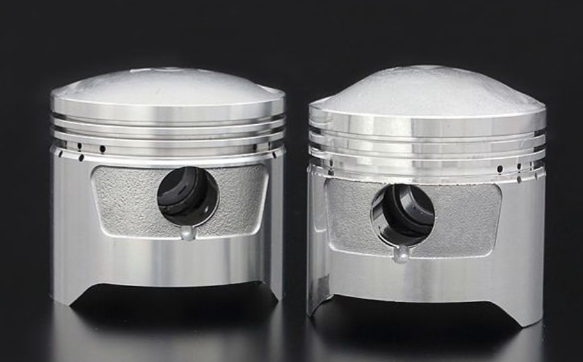 Two metallic piston-like objects on a reflective surface with a dark background