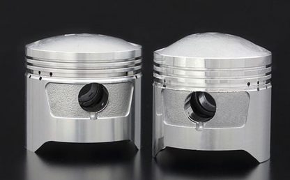 Two metallic piston-like objects on a reflective surface with a dark background