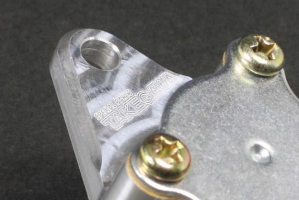 Metal component with screws and 'Takegawa' branding on a dark background
