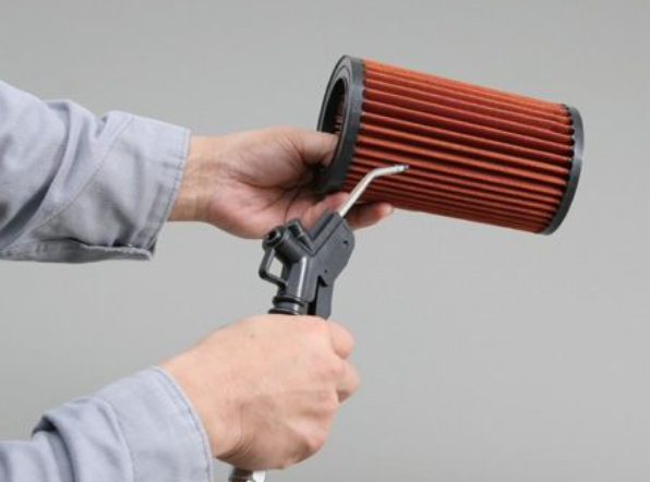 Person holding a red air filter and a high-pressure washer gun against a gray background