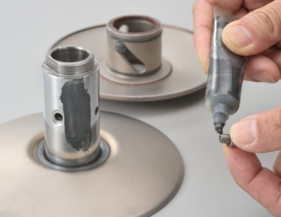 Person applying black material to metal components using a tube on a gray background