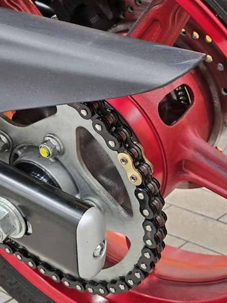 Close-up of a motorcycle chain and sprocket with red and black components.