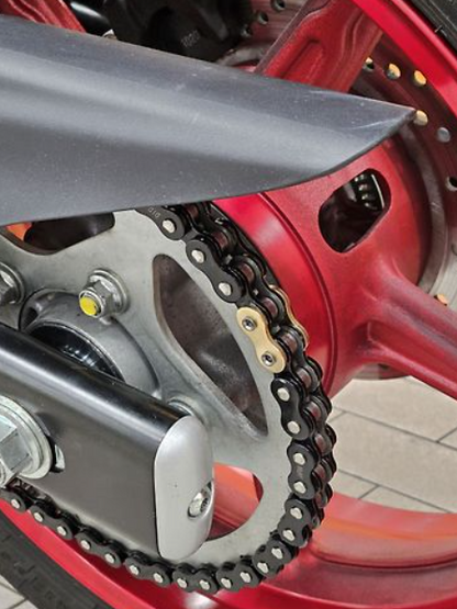 Close-up of a motorcycle chain and sprocket with red and black components.
