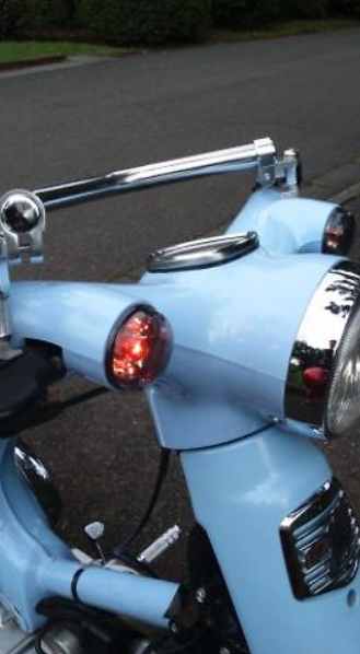Close-up of a light blue motorcycle with chrome details on a road.