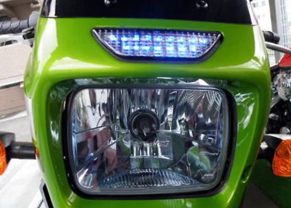 Close-up of a green motorcycle headlight with blue LED lights.