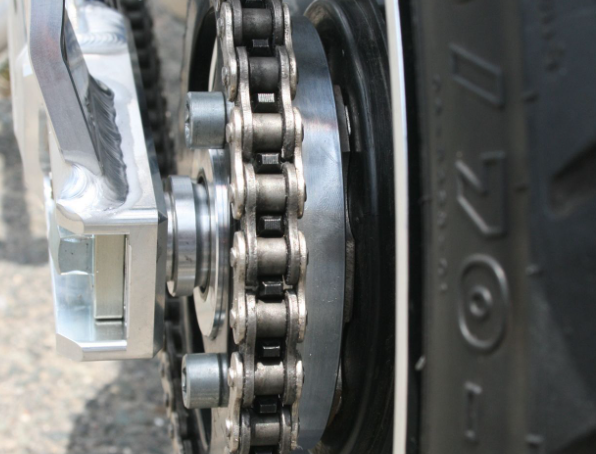 Close-up of a motorcycle chain and sprocket with a tire in the background
