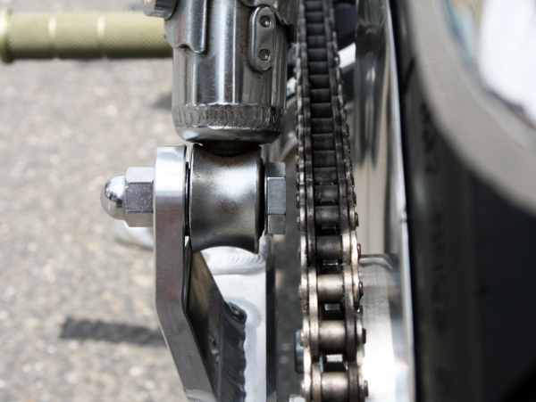 Close-up of a motorcycle chain and sprocket on a road.