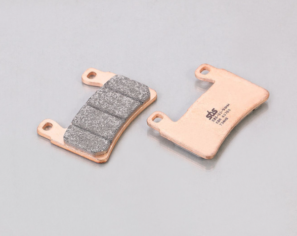 Two brake pads, one with a metallic finish and one with a textured surface, on a gray background.