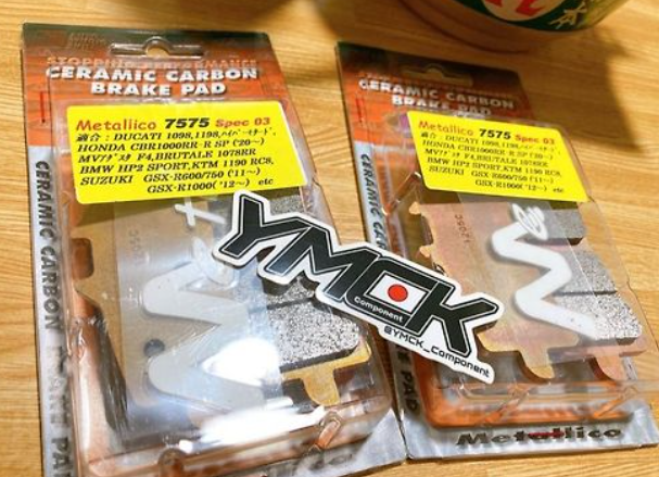 Two packages of YOKO ceramic carbon brake pads on a wooden surface.