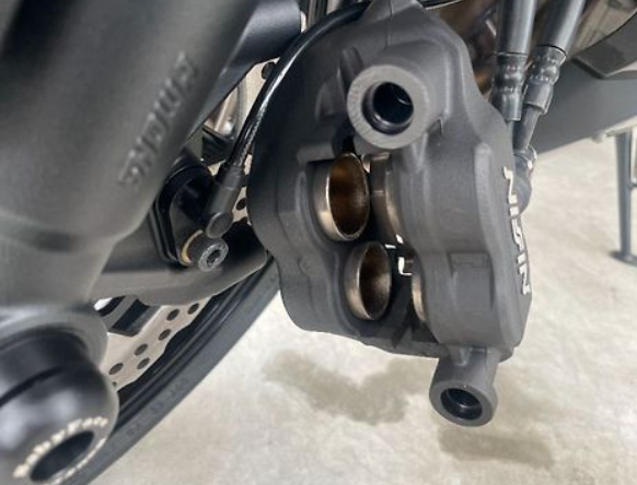Close-up of a motorcycle brake caliper and rotor on a light background