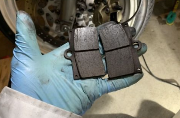 Person wearing a blue glove holding brake pads near a motorcycle wheel.