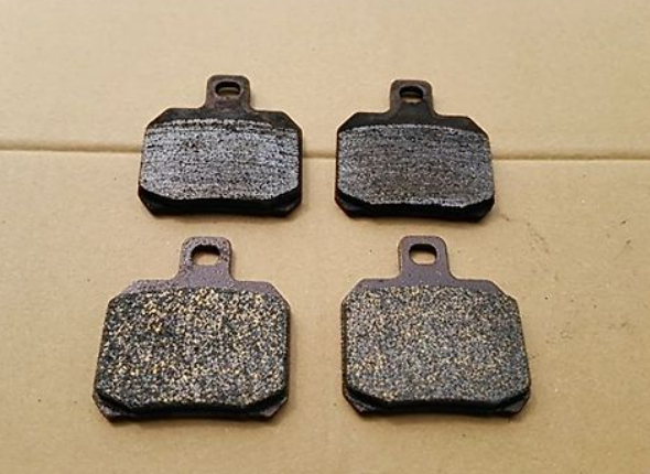 Four black brake pads on a beige background