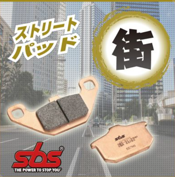 Two brake pads with SBS branding on a blurred cityscape background
