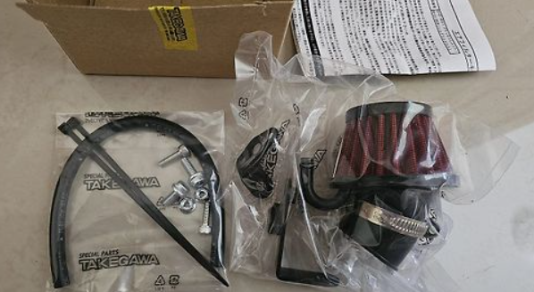 Automotive parts including a air filter and hose on a cardboard box with Takegawa branding.