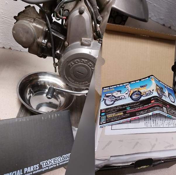 Motorcycle engine on a stand with a box and parts manual in the background