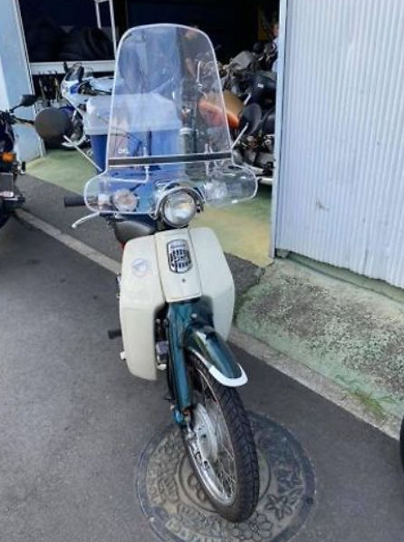 White scooter with a clear windshield parked on a concrete surface.