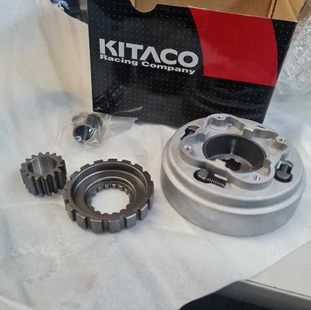 Mechanical parts on a white surface with a Kitaco Racing Company box in the background.