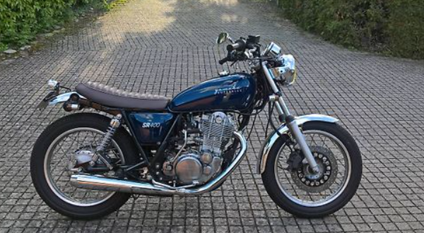 Blue motorcycle on a paved driveway with greenery in the background