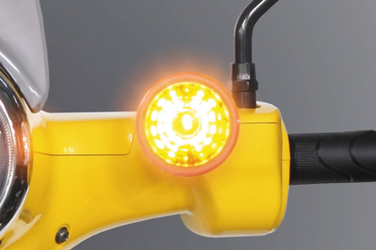 Close-up of a yellow motorcycle handlebar with an illuminated turn signal against a gray background