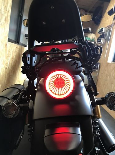 Close-up of a motorcycle's taillight with a red light on, set against a blurred indoor background.