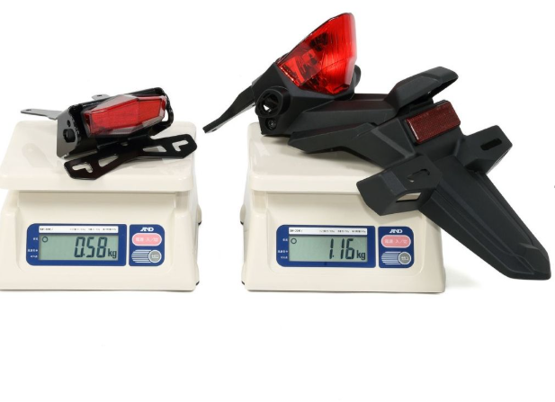 Two motorcycle taillights on digital scales with weight readings displayed.