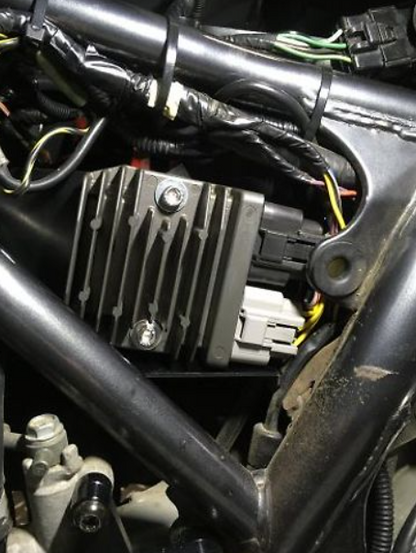Close-up of a motorcycle's electrical components including a regulator and wiring.
