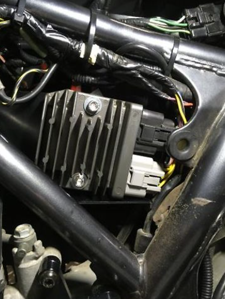 Close-up of a motorcycle's electrical components including a regulator and wiring.