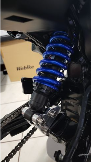 Close-up of a motorcycle suspension system with blue spring and Webike branding.