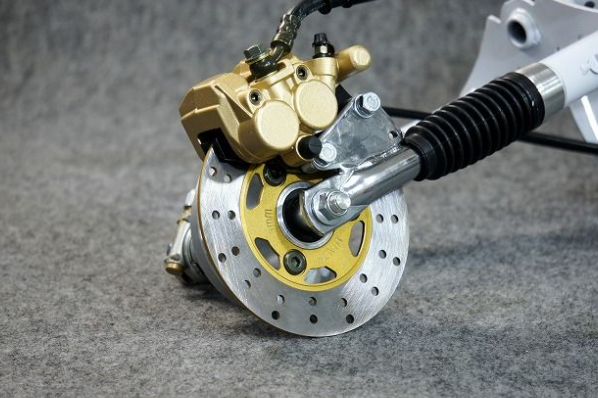 Close-up of a motorcycle brake system with gold and silver components on a gray background