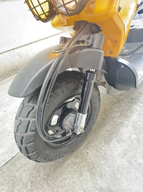 Close-up of a scooter's front wheel and suspension on a concrete surface.