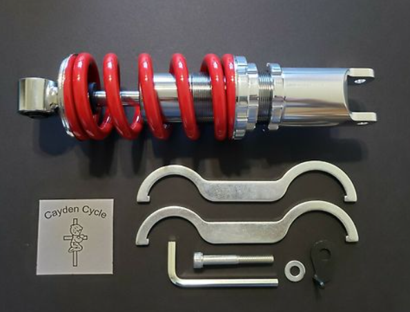 Motorcycle shock absorber with red spring and metal components on a black background, featuring 'Cayden Cycle' branding.