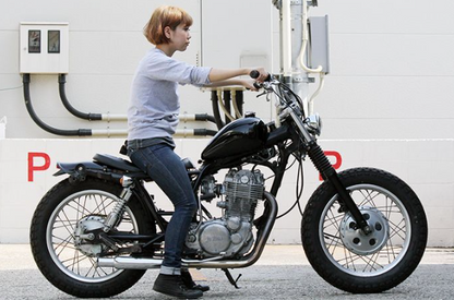 Person sitting on a motorcycle in front of a building with visible branding.